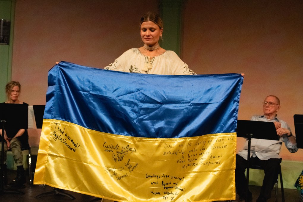 Daria Kolomiec en la lectura del «Diary of War» del 2 de junio de 2024, junto a la bandera ucraniana con la inscripción «La felicidad favorece a los valientes», escrita por Iryna «Cheka» Tsybukh, que firmó la bandera pocas semanas antes de su muerte. Foto: Anastasia Krasheninnikova Daria Kolomiec en la lectura del «Diary of War» del 2 de junio de 2024, junto a la bandera ucraniana con la inscripción «La felicidad favorece a los valientes», escrita por Iryna «Cheka» Tsybukh, que firmó la bandera pocas semanas antes de su muerte. Foto: Anastasia Krasheninnikova
